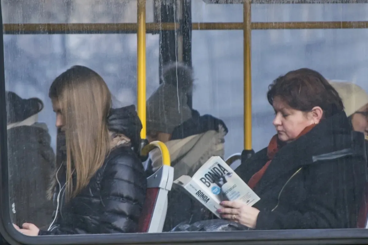 Women seated on public transport, one reading a newspaper